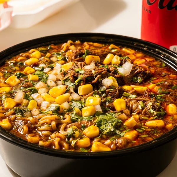 A large bowl of chili with corn, diced onions, and cilantro, next to fries and a soda.